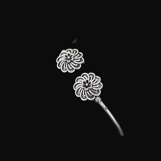 Silver floral earrings on a gray cushion with a dark background