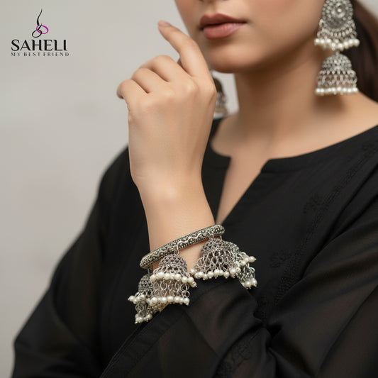 Silver and pearl earrings on a black stand with 'SAHELI' branding.