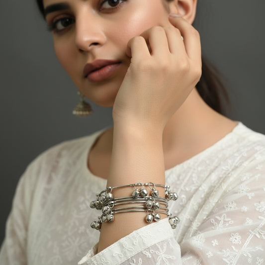 Set of silver anklets with small bells on a dark gray stand, brand 'Saheli' visible.