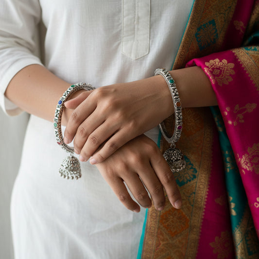 Pair of silver bangles with colorful stones on a dark surface