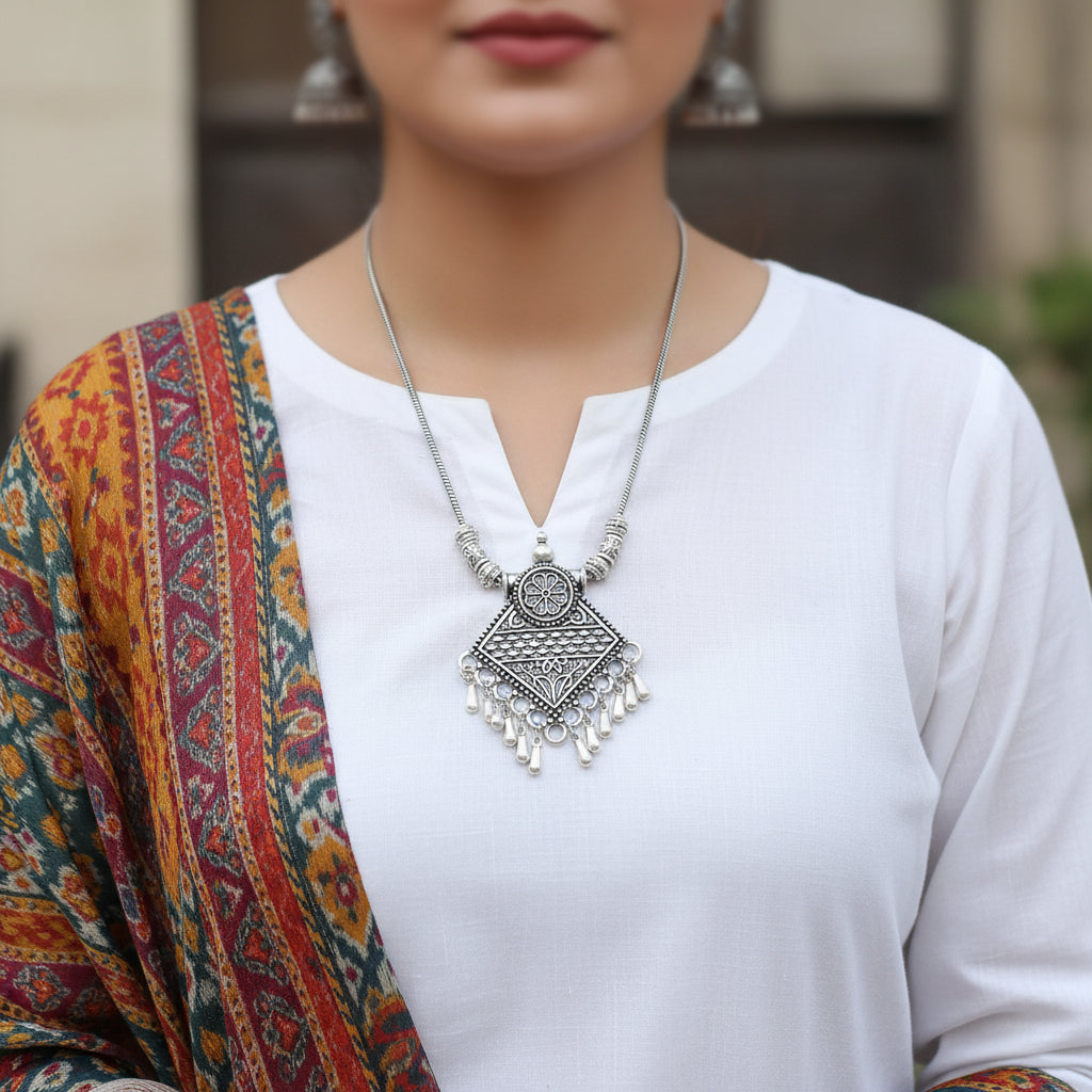 Silver necklace with intricate pendant on a gray background, featuring the brand 'Saheli'.