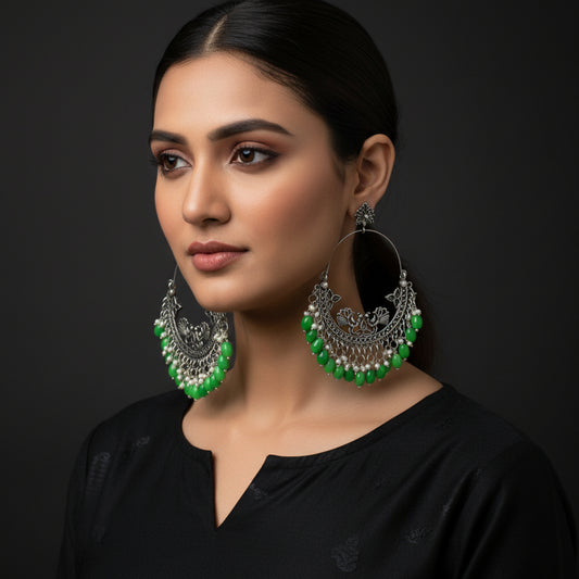 Ornate hoop earrings with green beads on a dark background