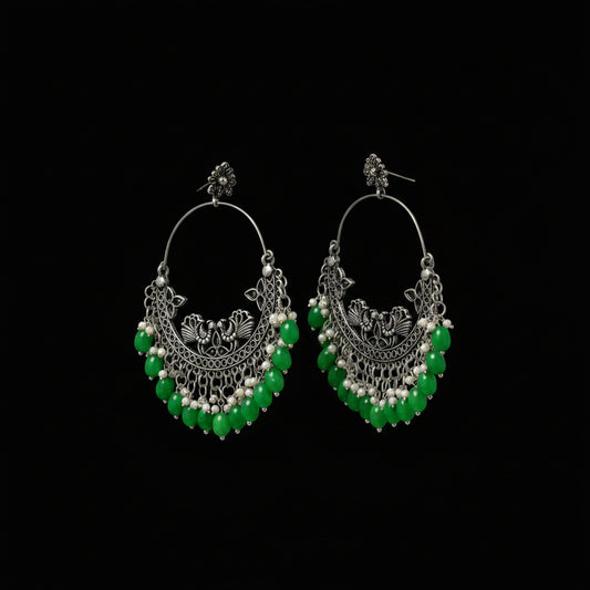 Ornate hoop earrings with green beads on a dark background