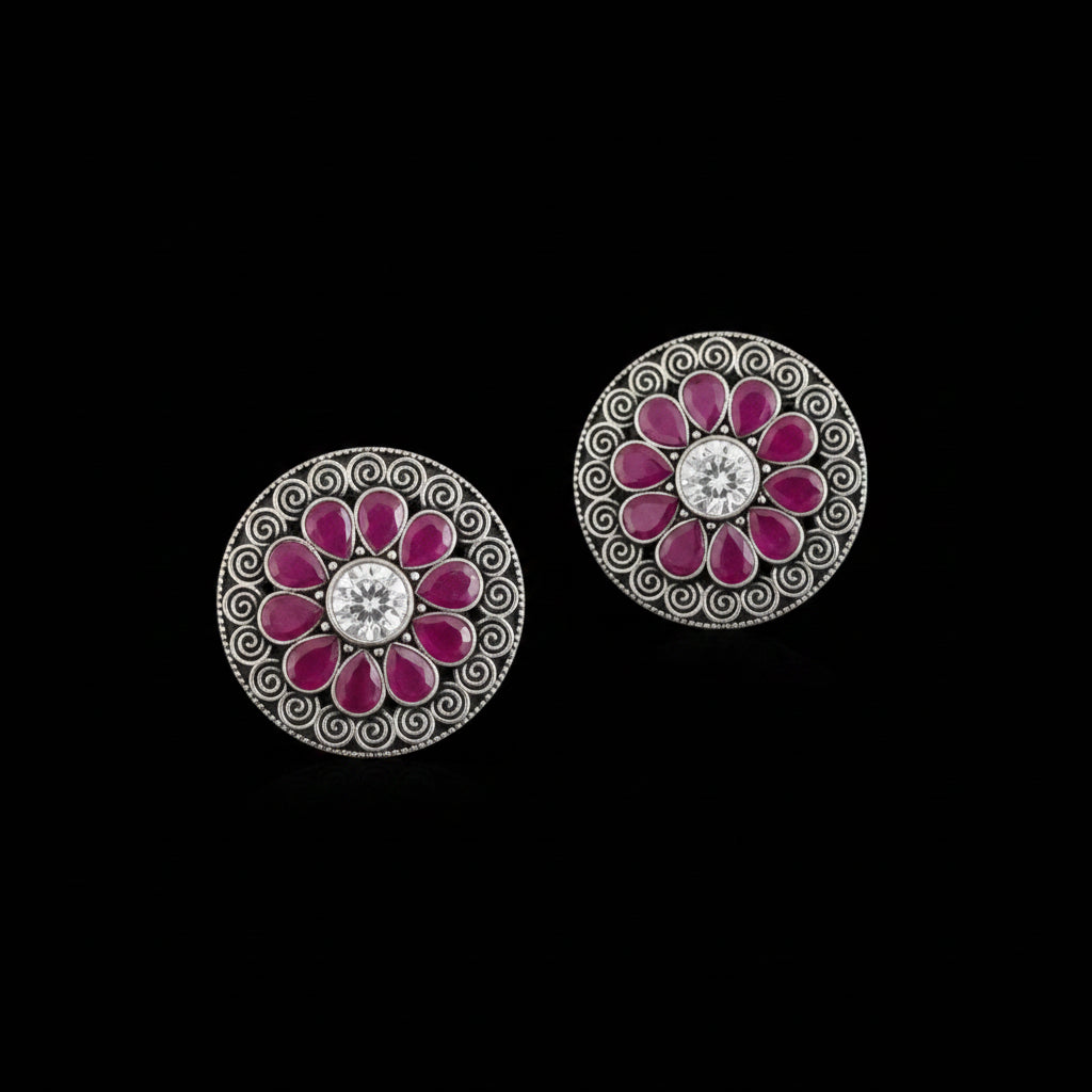 Pair of floral earrings with pink petals and a central gemstone on a gray background, branded 'SAHELI'.