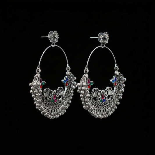 Pair of silver hoop earrings with colorful gemstones on a gray stand against a dark background