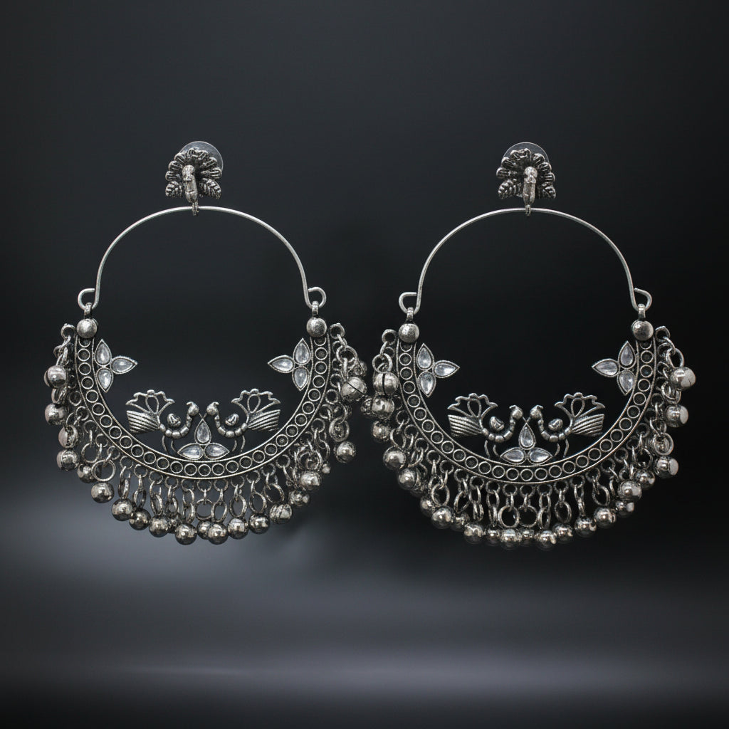 Pair of silver hoop earrings with intricate designs on a gray stand against a dark background