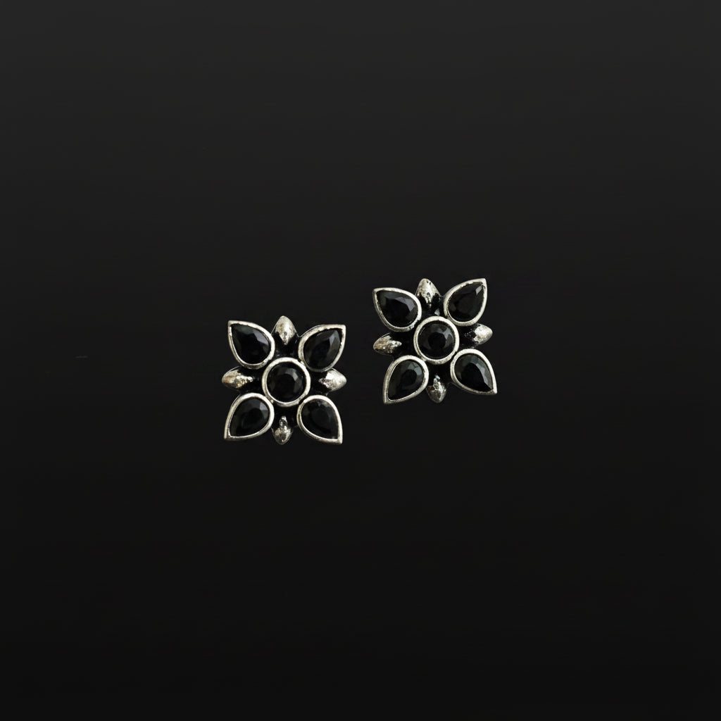 Pair of silver flower-shaped earrings with black centers on a reflective surface.