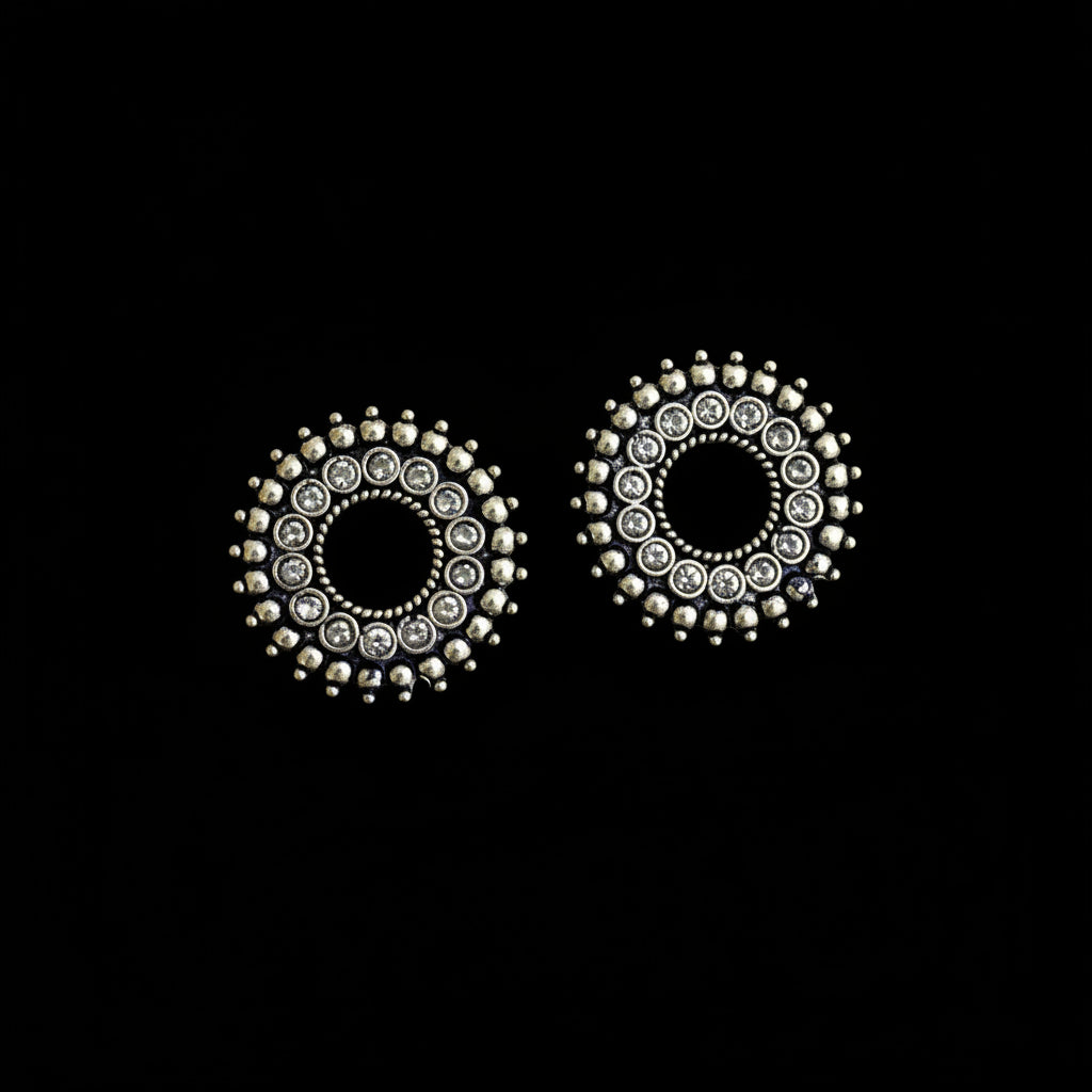 Pair of round earrings with metallic and gemstone details on a dark background