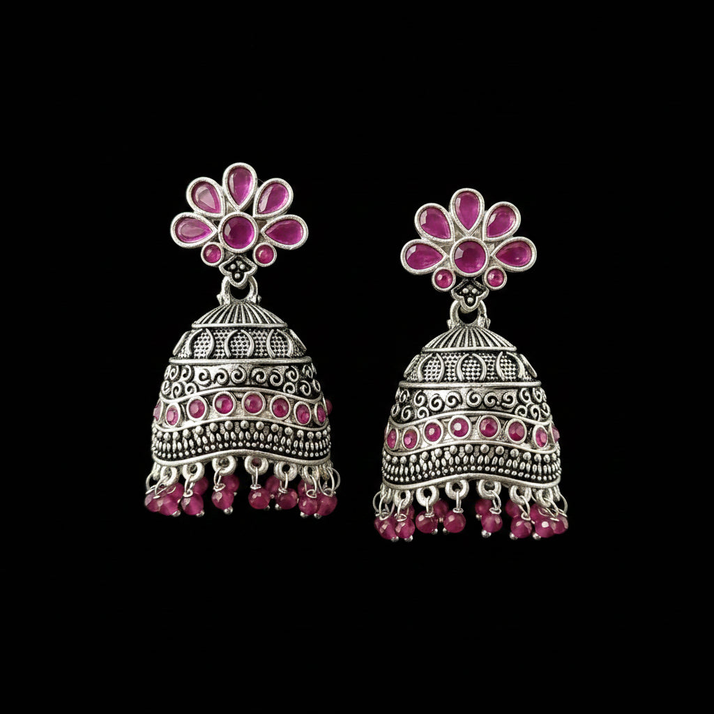 A pair of silver-toned Indian jhumka earrings with pink stone accents, displayed on a gray stand against a light gray background.