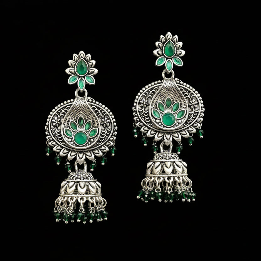 Ornate silver earrings with green gemstones on a gray stand.