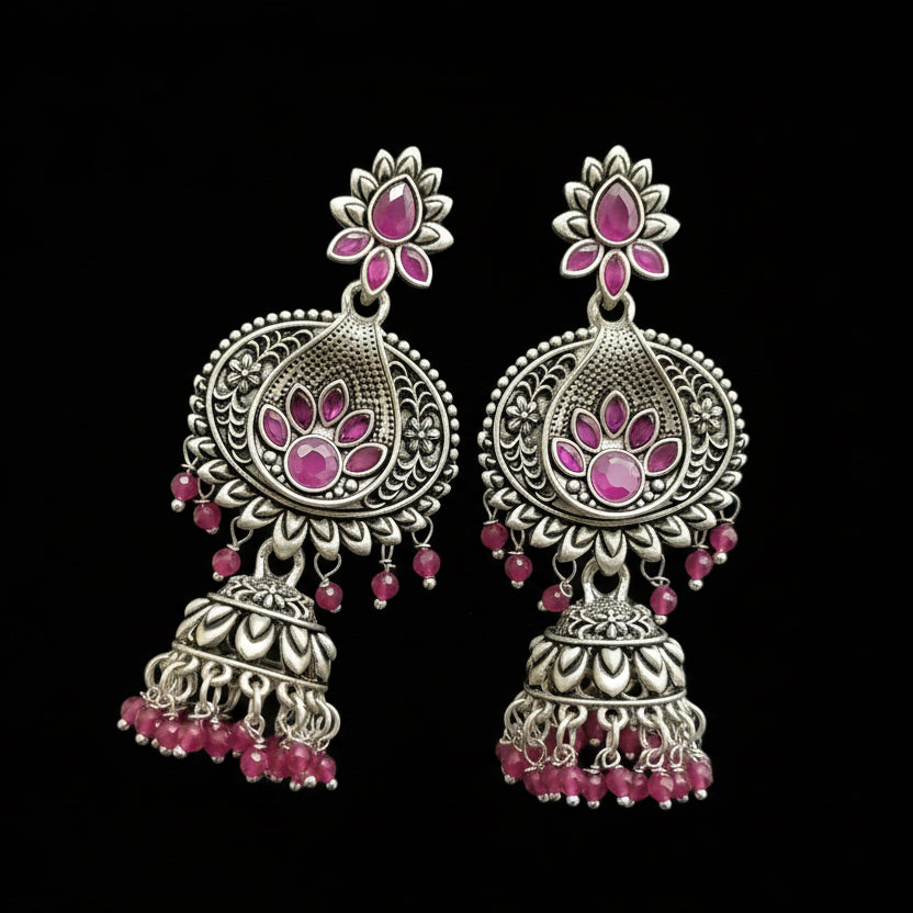 Ornate silver earrings with pink gemstones on a gray stand.