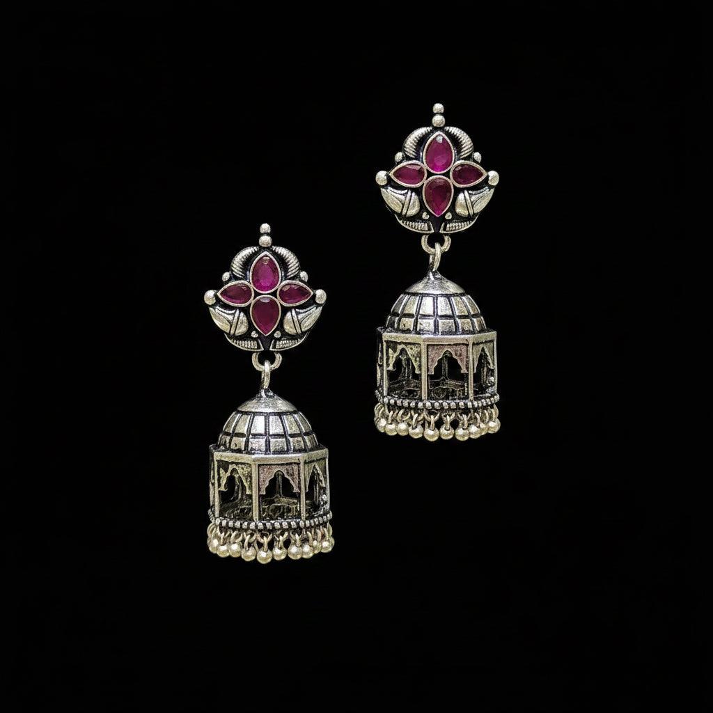 Ornate silver earrings with red gemstones on a black stand against a gray background