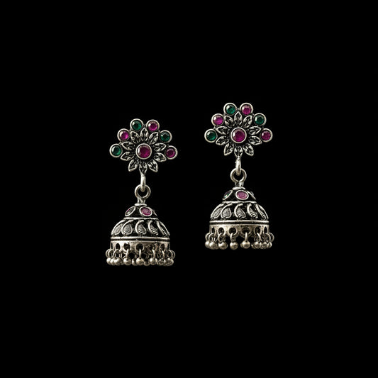 Ornate earrings with gemstones on a gray stand, branded 'Saheli'.