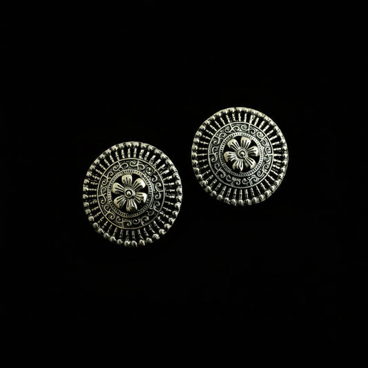 A pair of round silver-toned metal buttons with intricate floral and geometric filigree detailing, displayed on a dark reflective surface.