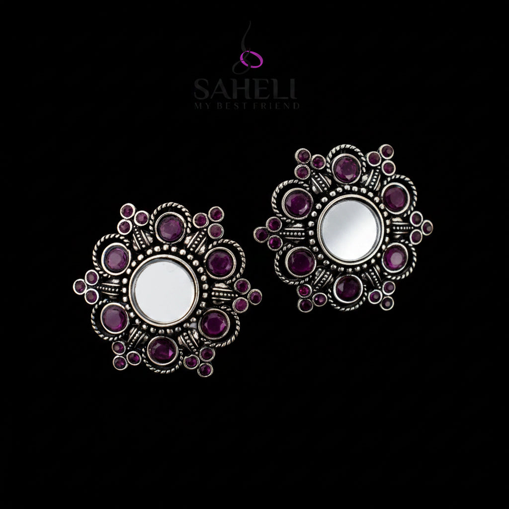 Ornate silver and purple earrings on a gray background with 'Saheli' branding.