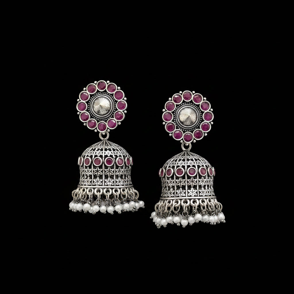 Silver jhumka earrings with pink gemstones on a gray stand.