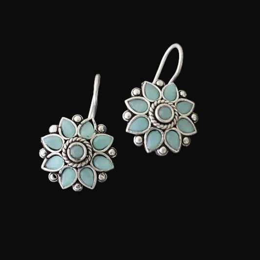 Pair of turquoise flower-shaped earrings on a gray stone surface