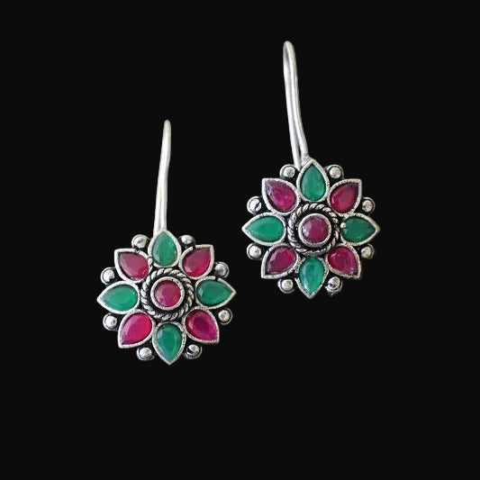 Floral earrings with green and pink accents on a gray stone surface