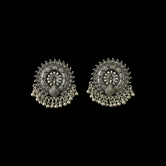 A pair of ornate silver-toned Indian jhumka earrings with intricate filigree work, floral motifs, and dangling bead chains, displayed on a dark reflective surface.