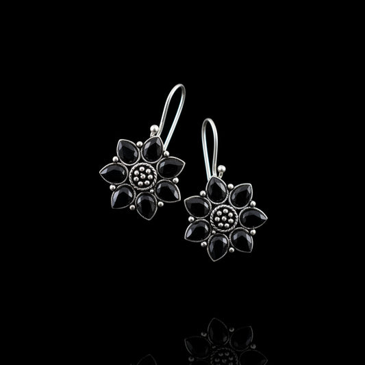 Pair of silver flower-shaped earrings on a gray cushion with a gray background