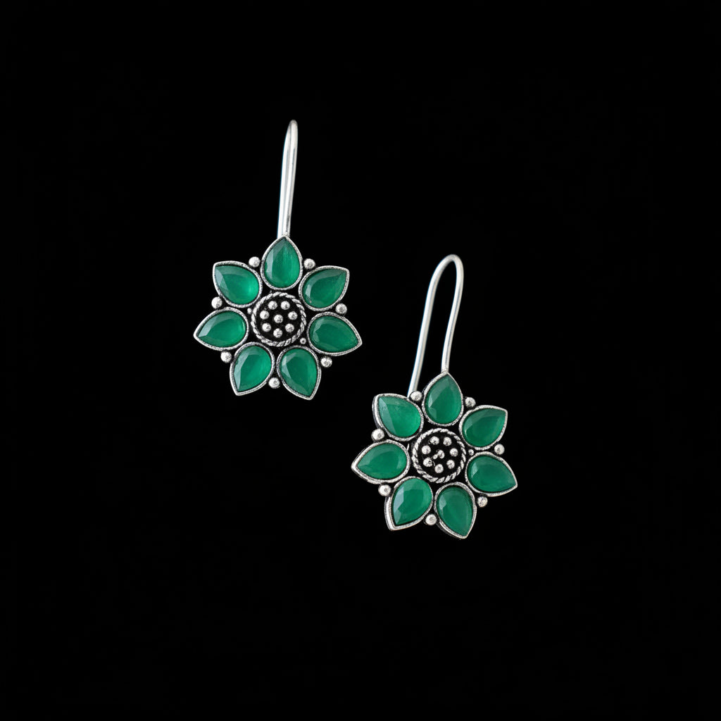Flower-shaped earrings with green petals and silver accents on a gray surface.