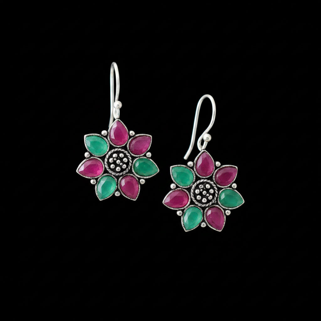 Flower-shaped earrings with green and pink petals on a gray cushion