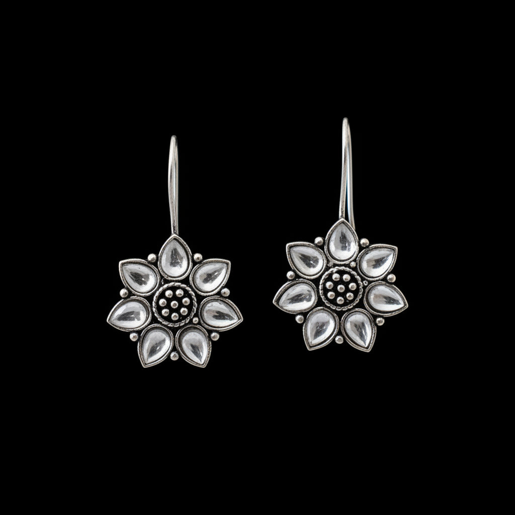 Pair of silver flower-shaped earrings on a gray cushion with a dark background