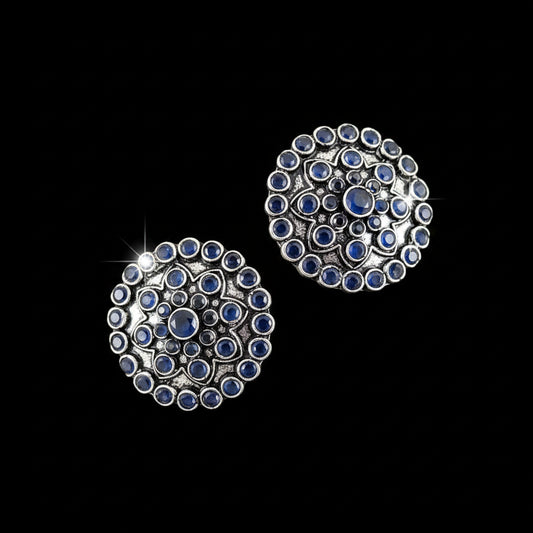 Pair of silver earrings with blue stones on a gray background, branded 'Saheli'.