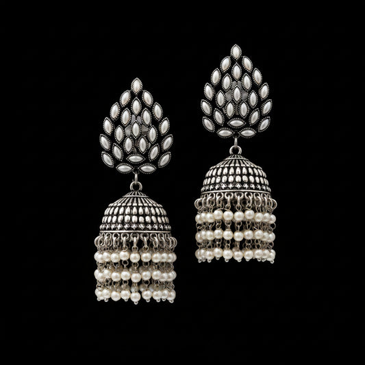 A pair of traditional Indian silver-toned jhumka earrings with white pearl bead fringe, displayed on a black stand against a white background. The brand logo 'SAHELI MY BEST FRIEND' is visible in the top left corner.