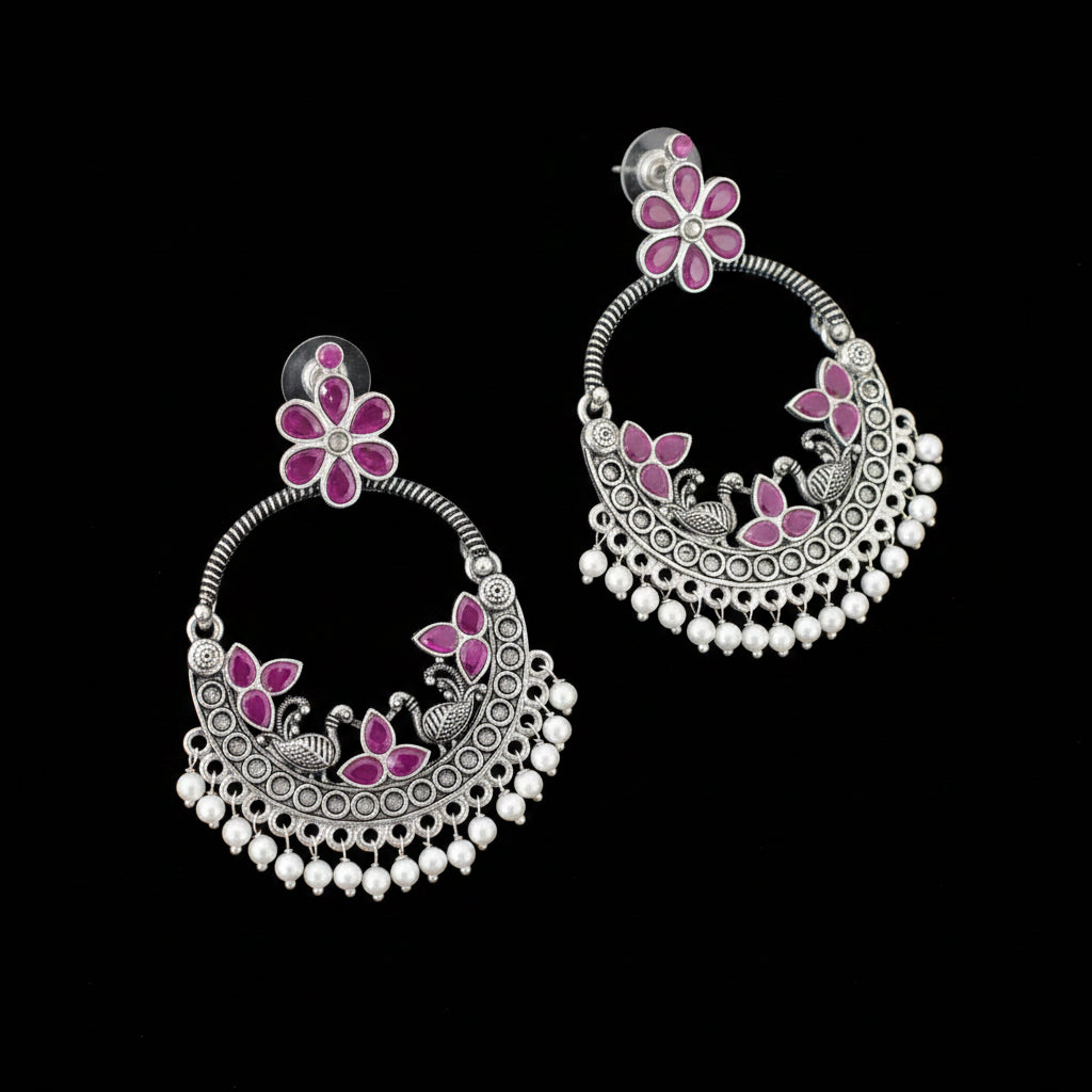 Ornate silver earrings with pink floral designs on a dark background