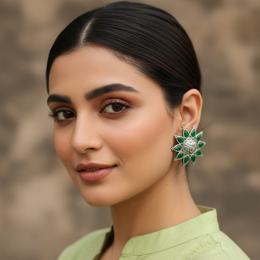 Pair of green and silver earrings on a blue textured surface with 'Al-Rawnaq' branding.