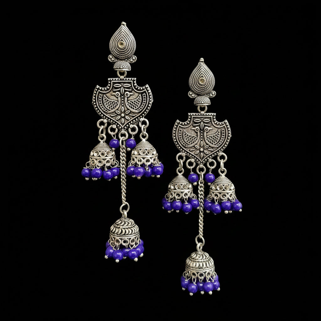 A pair of traditional Indian silver-toned jhumka earrings with purple beaded accents, displayed on a gray Y-shaped stand against a light gray background with the brand name 'SAHELI MY BEST FRIEND' at the top.