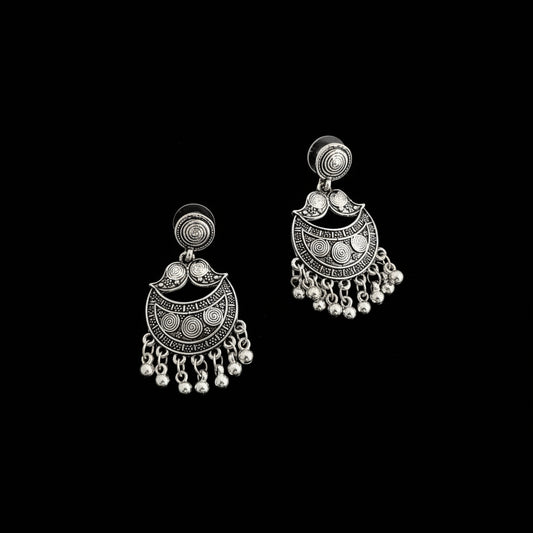 A pair of silver-toned traditional Indian jhumka earrings with intricate filigree work and dangling bead chains, displayed on a dark reflective surface.