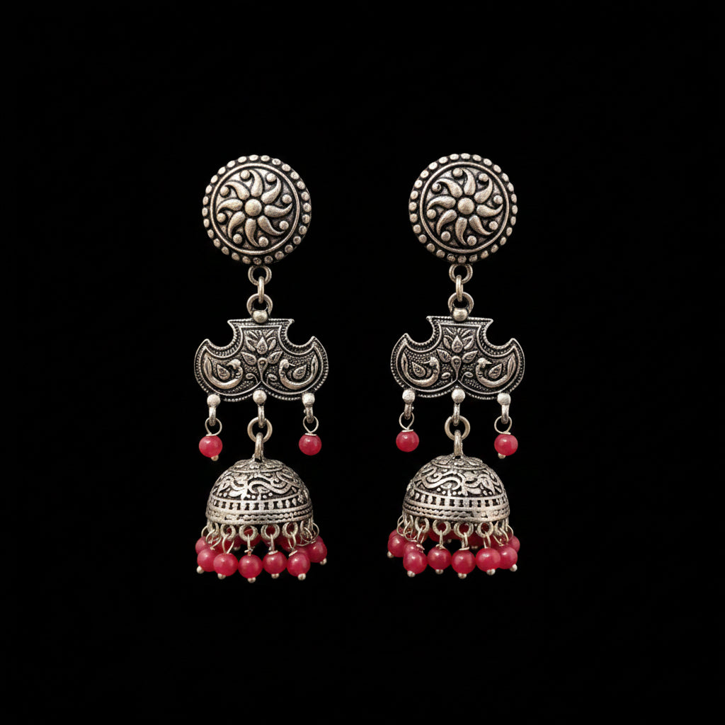A pair of traditional Indian silver-toned jhumka earrings with red bead accents, displayed on a gray Y-shaped stand against a neutral gray background. The brand logo 'SAHELL MY BEST FRIEND' is visible at the top center.