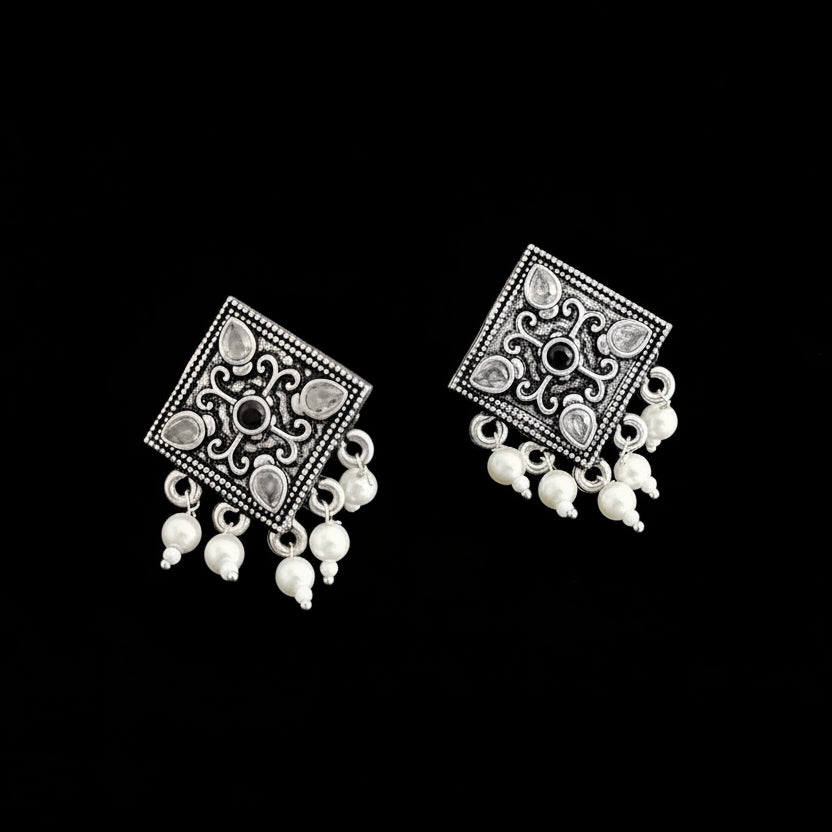 Pair of silver earrings with square designs and white beads on a dark background