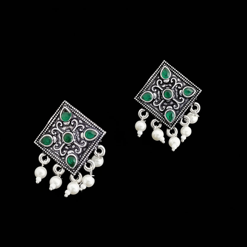 Pair of silver earrings with green gemstones and white beads on a gray background