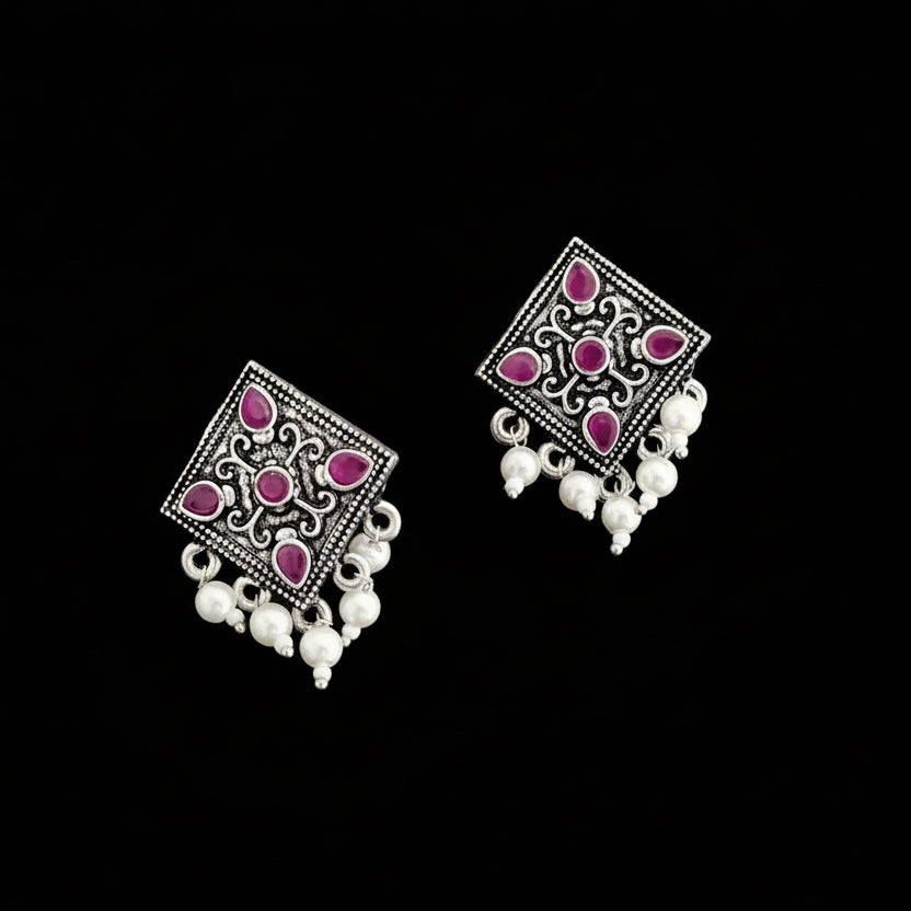 Pair of square-shaped earrings with pink gemstones and white beads on a gray background