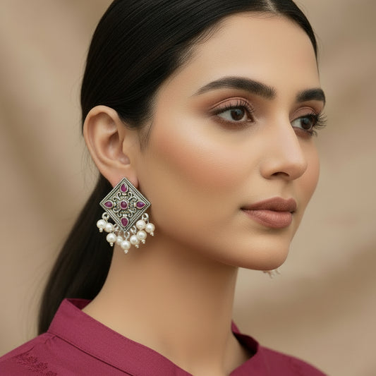 Pair of square-shaped earrings with pink gemstones and white beads on a gray background