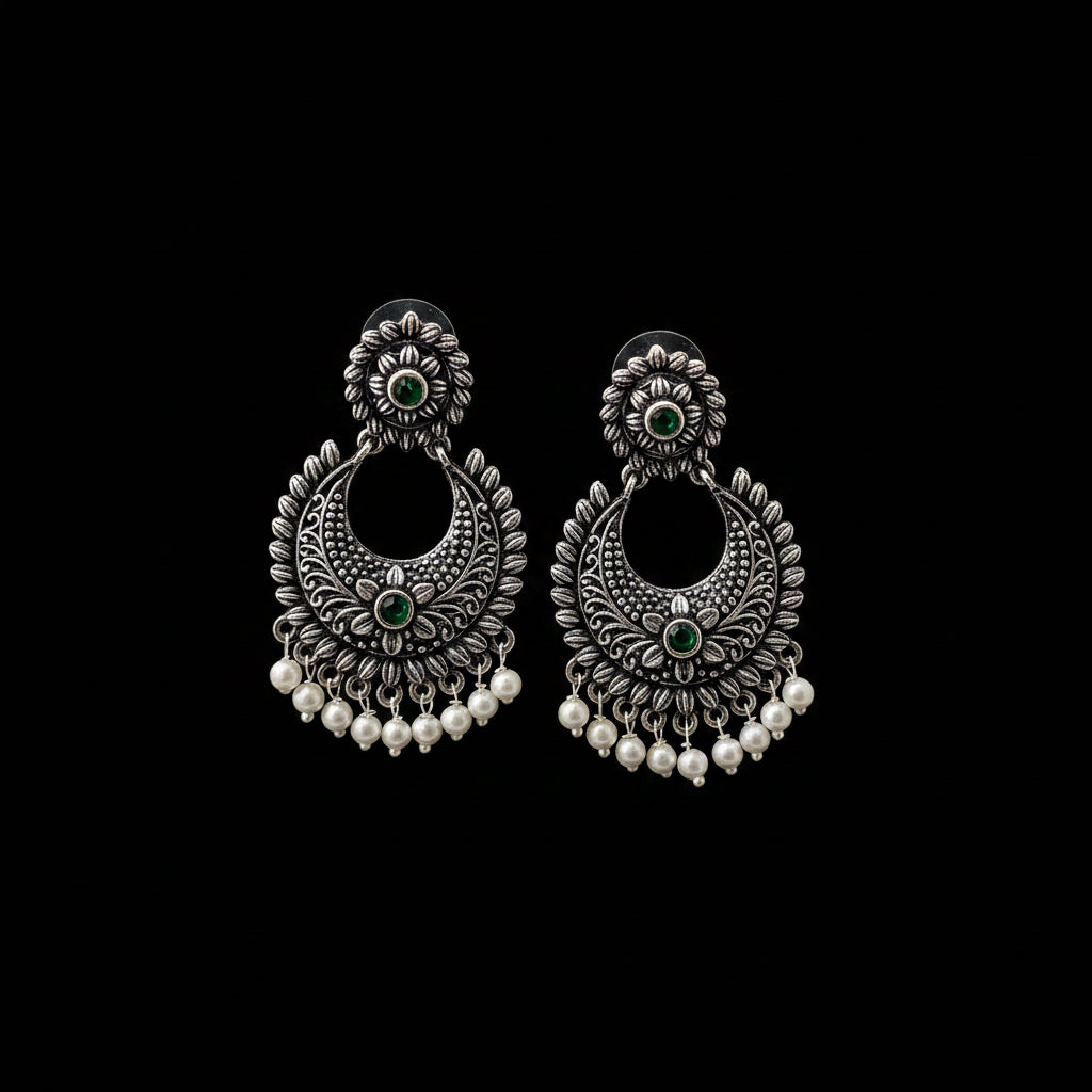 Pair of silver earrings with green stones and pearl-like beads on a gray background, branded 'Saheeli'.