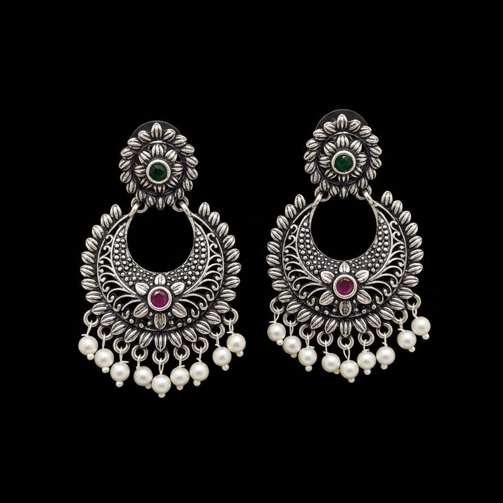 Pair of silver earrings with pearls and gemstones on a gray background, branded 'Saheli'.