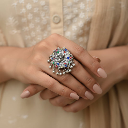 Decorative ring with multicolored gemstones on a black mannequin hand against a dark background