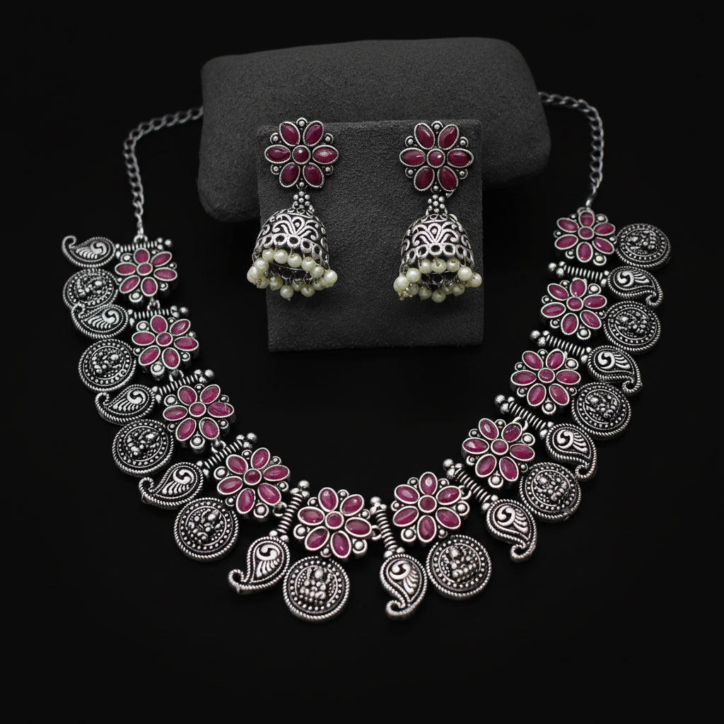 Silver necklace with pink floral designs and matching earrings on a gray background