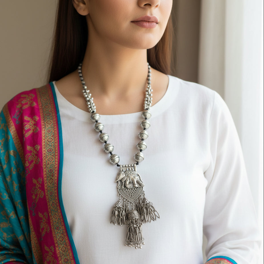 Silver necklace with elephant pendant on a gray background, featuring the brand 'Saheli'.