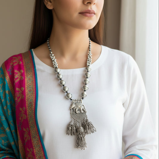 Silver necklace with elephant pendant on a gray background, featuring the brand 'Saheli'.