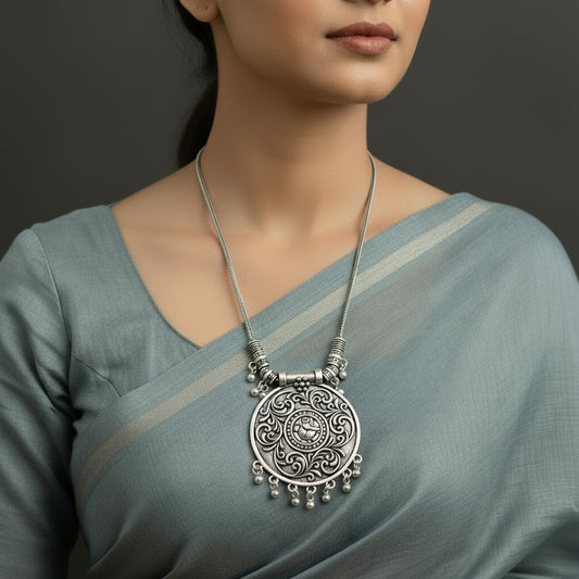 Silver necklace with intricate pendant on a dark background, featuring the brand 'Saheli'.