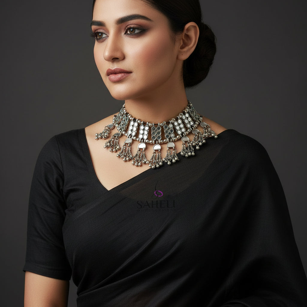 Silver necklace with dangling beads on a black background, featuring the brand 'Saheli'.