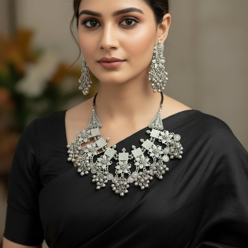 Silver jewelry set with necklace and earrings on a gray background, featuring the brand 'Saheli'.