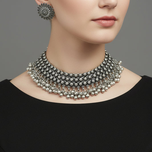 Silver necklace and earrings set on a reflective surface with 'Saheli' branding.