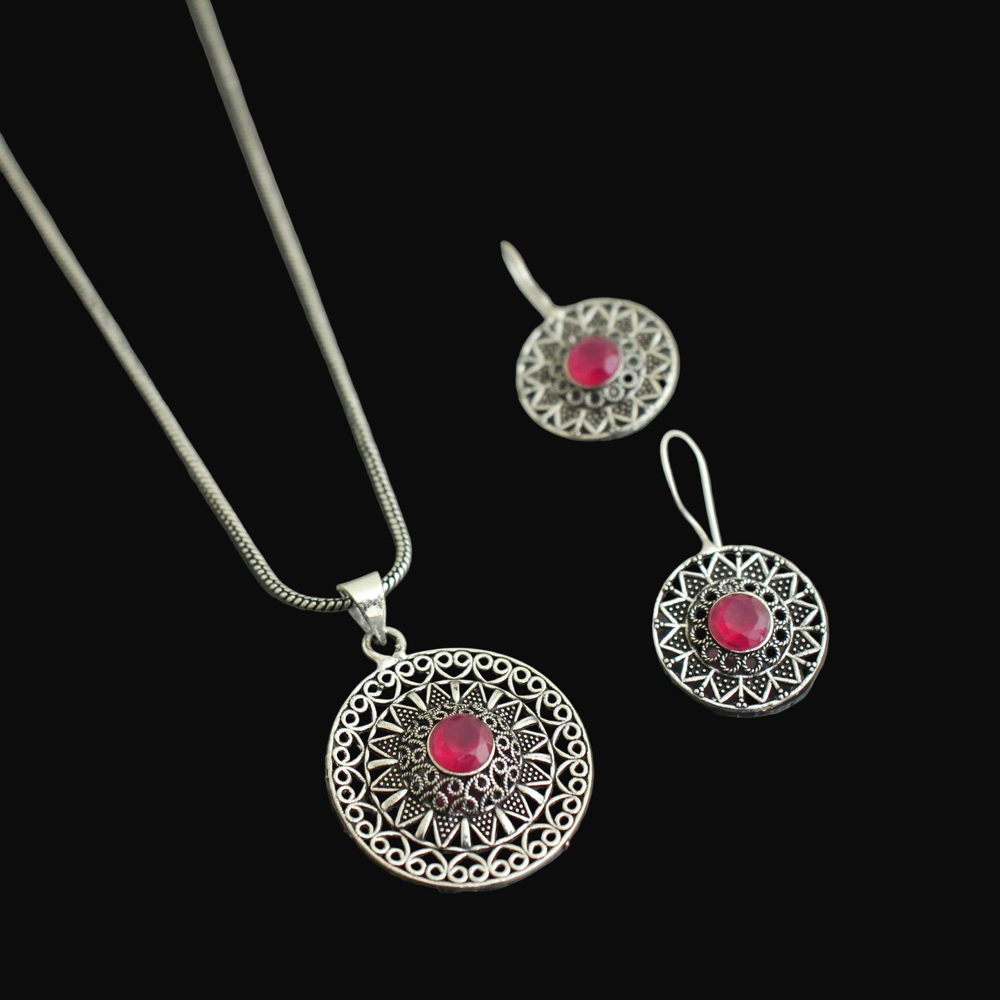 Silver jewelry set with red gemstones on a dark surface