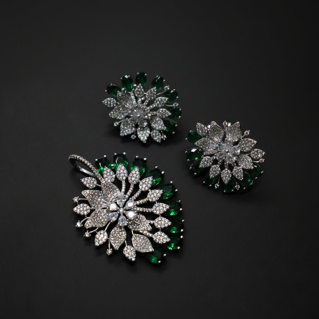 Three floral jewelry pieces with green and clear gemstones on a gray background